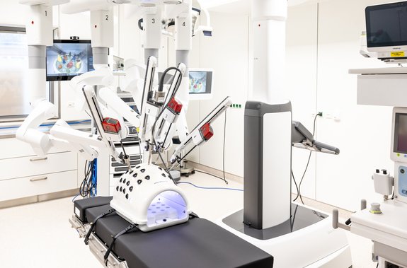 Ein Operationssaal, auf dem OP-Tisch ein ovaler Gegenstand, in dem mehrere Endoskope stecken. Im Hintergrund ein Bildschirm.