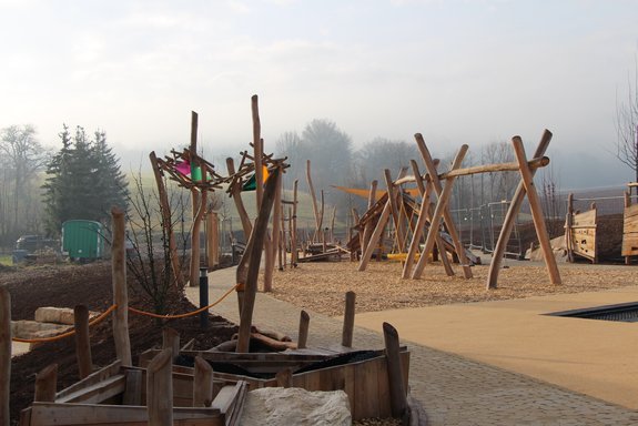 EIn Spielplatz mit vielen Spielgeräten aus Holz bei nebligem Wetter.