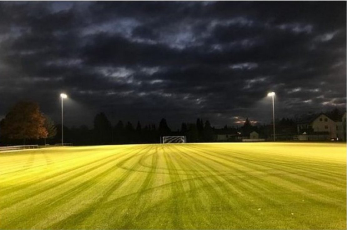 Ein leerer Fußballplatz bei Nacht, beleuchtet durch Flutlicht.