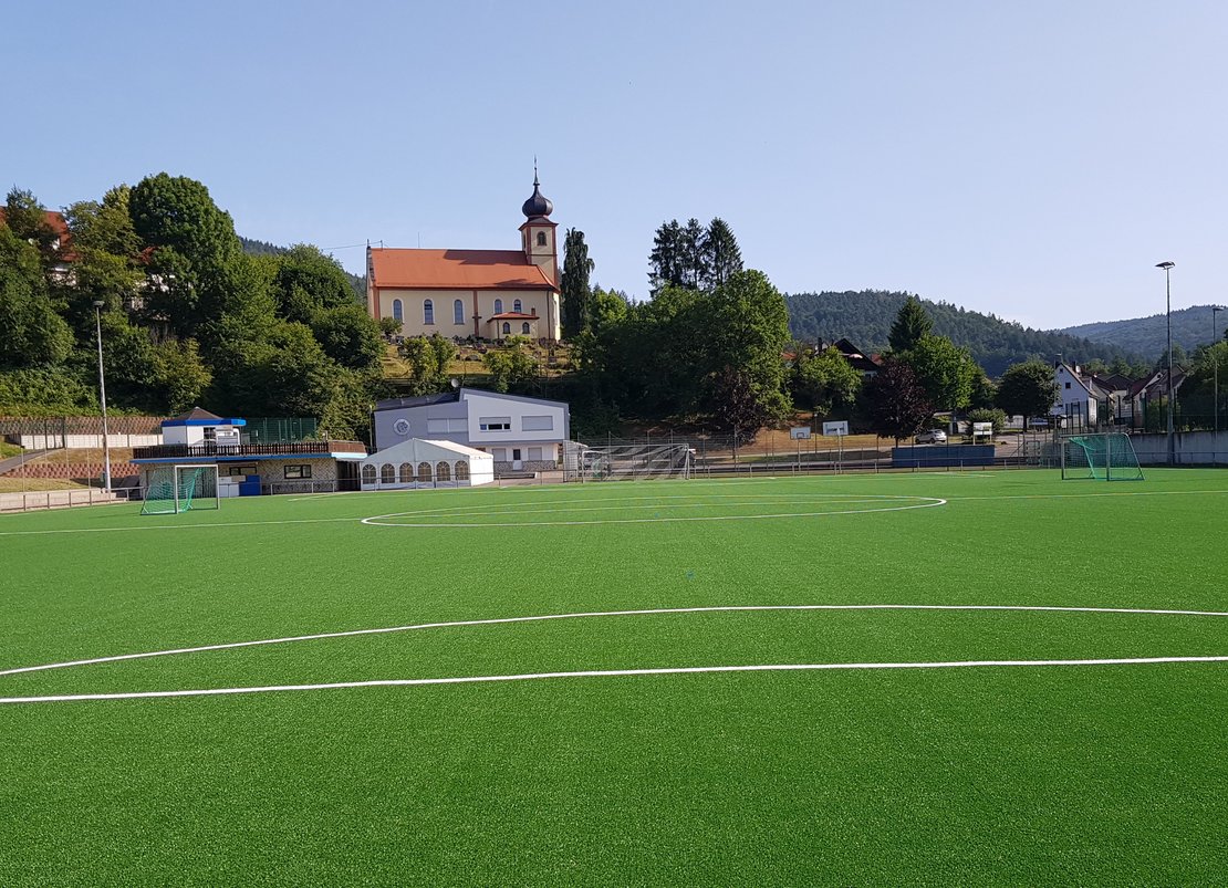 Ein Fußballfeld, im Hintergrund eine Kirche auf einem Hügel.