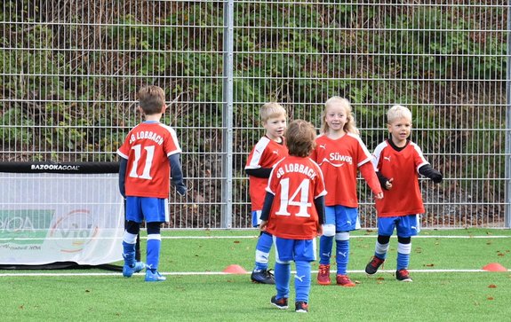 Fünf Kinder in roten Trikots spielen vor einem Mini-Fußballtor.