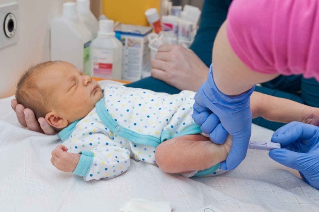 Einem Säugling wird ein Tropfen Blut aus der Ferse entnommen