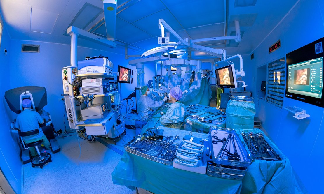Operationssaal mit viel Technik und einem Roboter, in blaues Licht getaucht