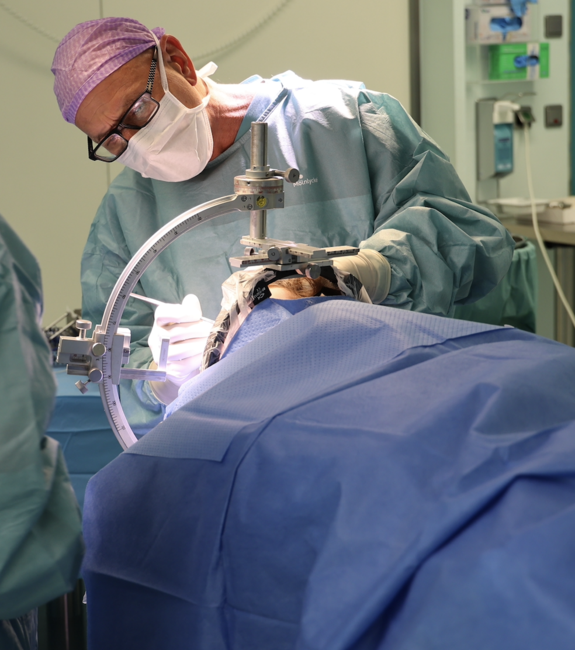 Ein Arzt operiert am Kopf eines Patienten, der durch ein Tuch verdeckt ist.