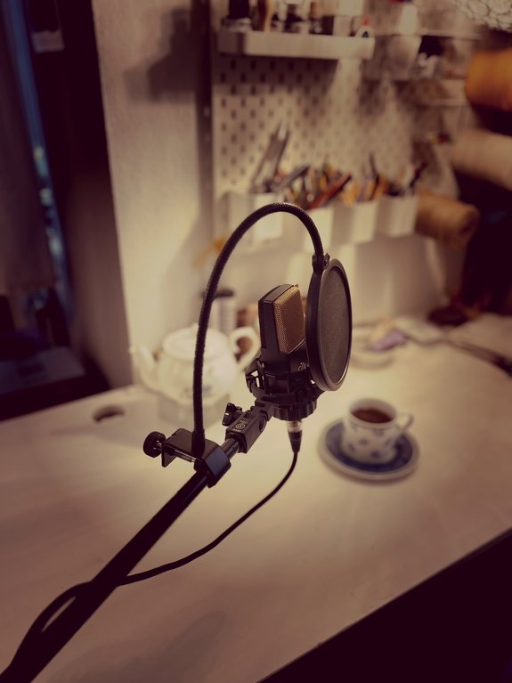Ein Mikrophon auf einem Schreibtisch. Im Hintergrund eine Tasse Tee und Schreibutensilien.