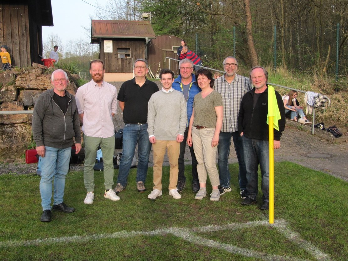 Acht Personen stehen an der Eckfahne eines Fußballfeldes.