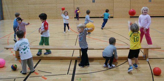 Kinder spielen in einer Sporthalle mit vielen bunten Bällen