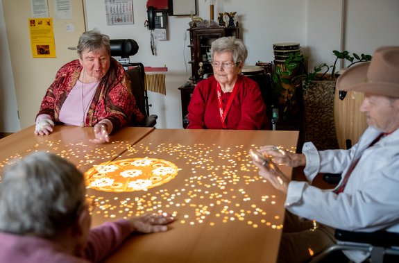 Vier Senioren sitzen um einen Tisch, auf den bunte Bilder projiziert werden.