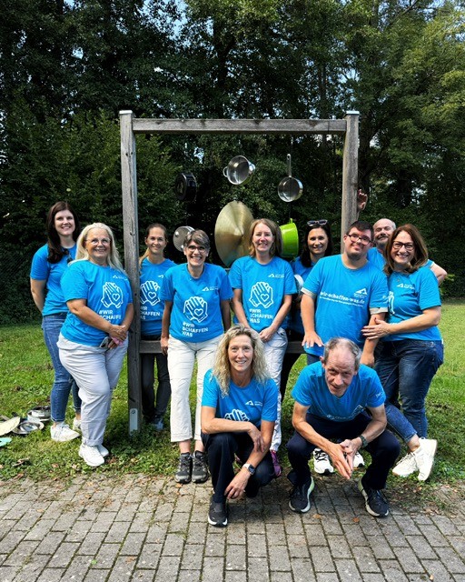 Mehrere Menschen in blauen T-Shirts stehen um ein Klangspiel herum.